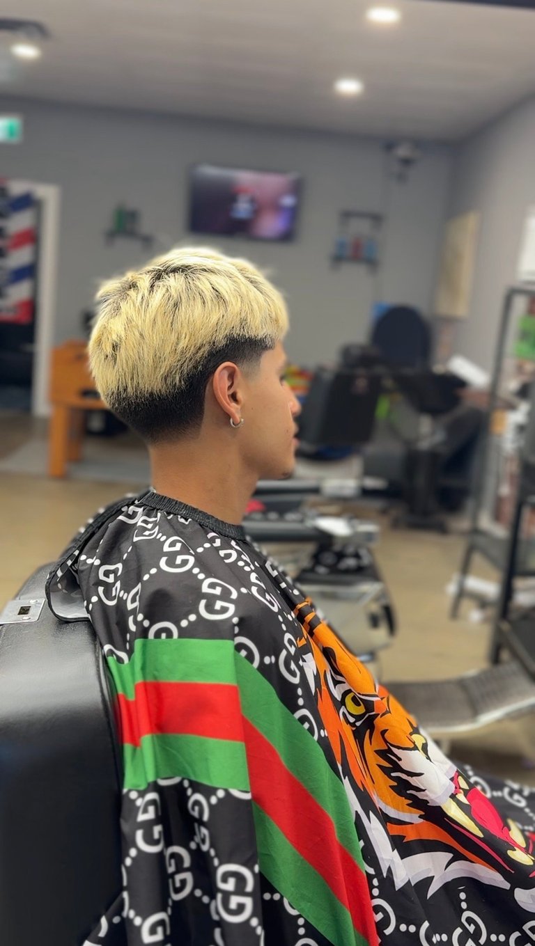 Person with platinum blonde undercut hairstyle wearing patterned black jacket in a salon setting