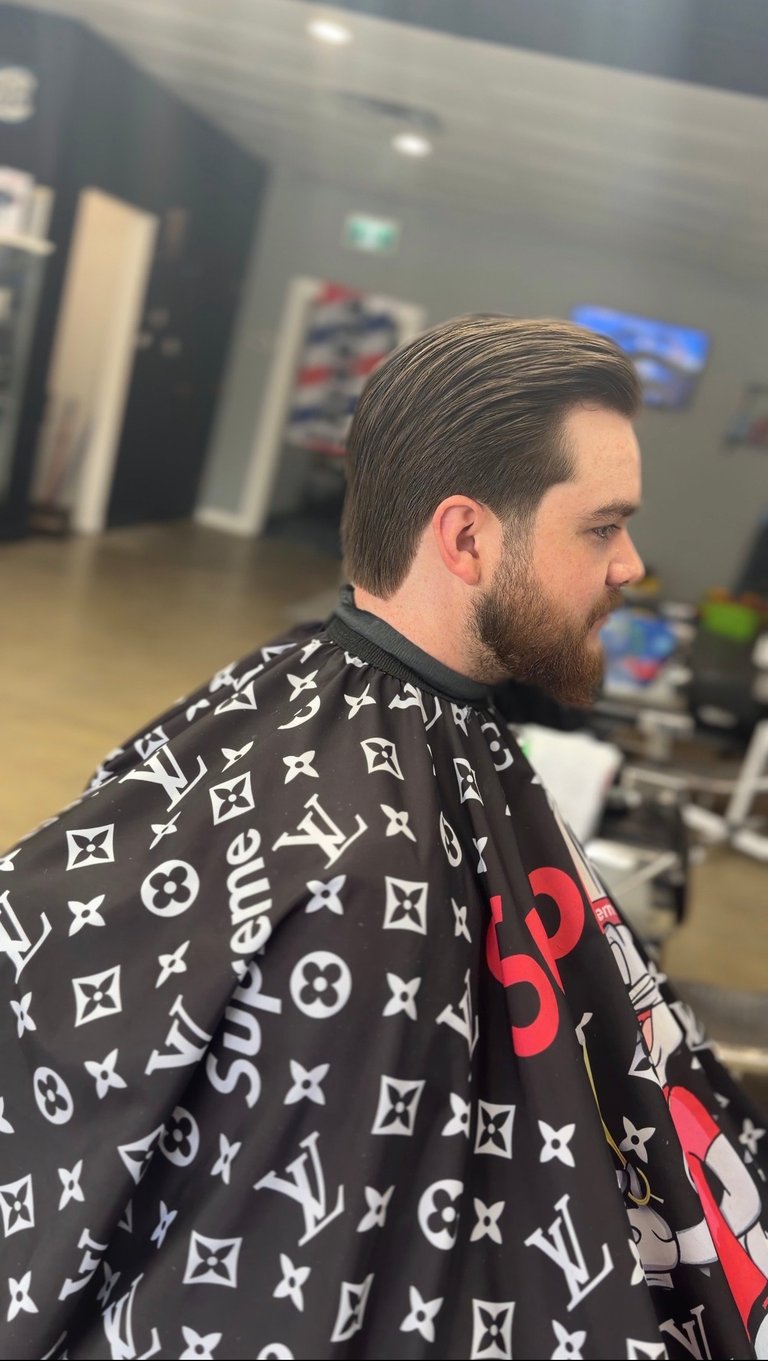 Man with beard in profile wearing black designer jacket with monogram pattern in barbershop setting